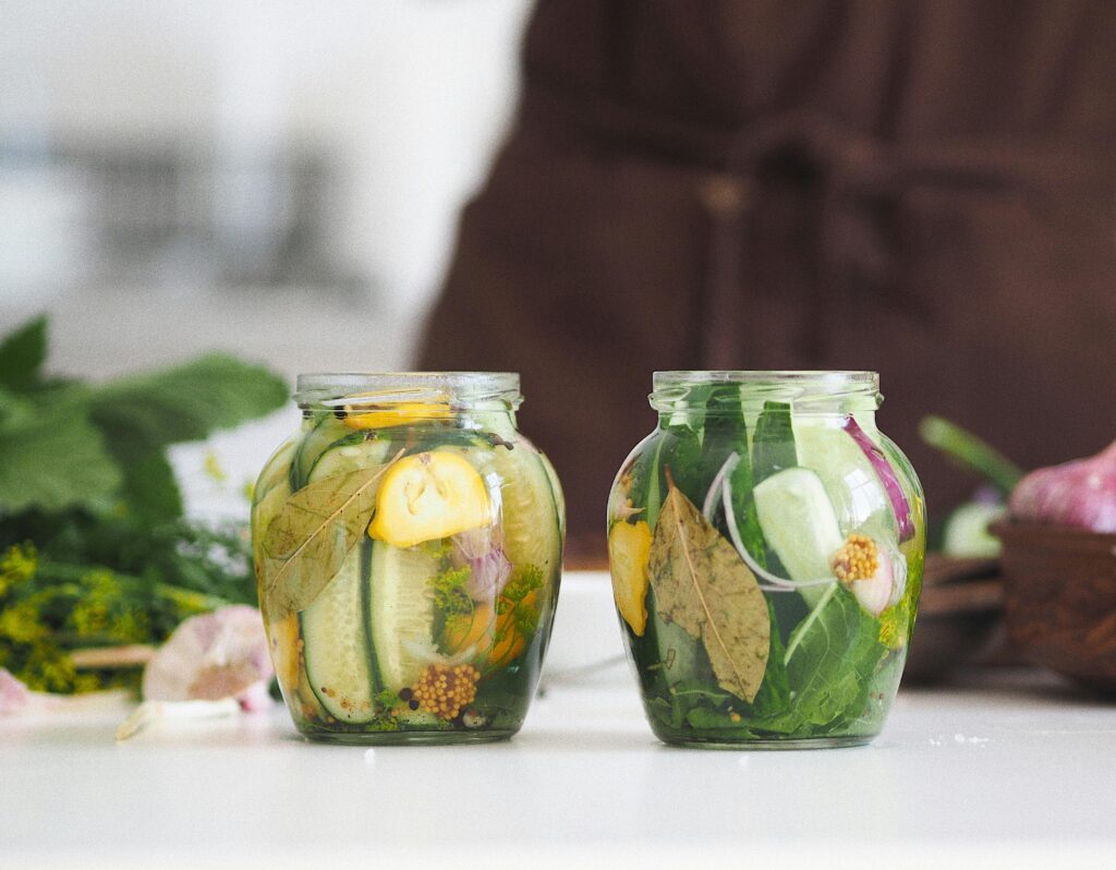 Two glass jars filled with homemade pickled cucumbers and herbs on a white kitchen surface.